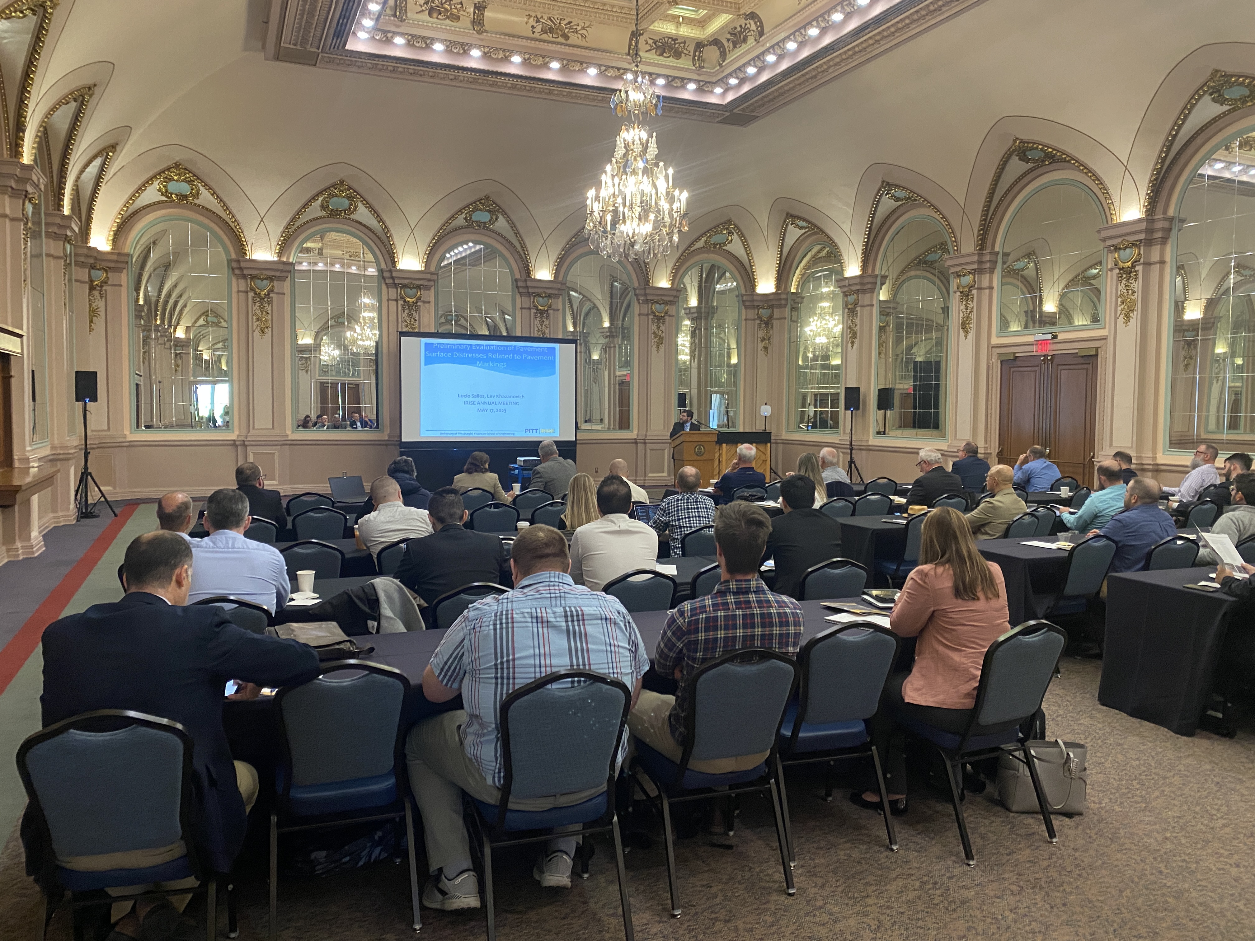 Members sitting at conference tables listening to a presenter at the irise annual meeting