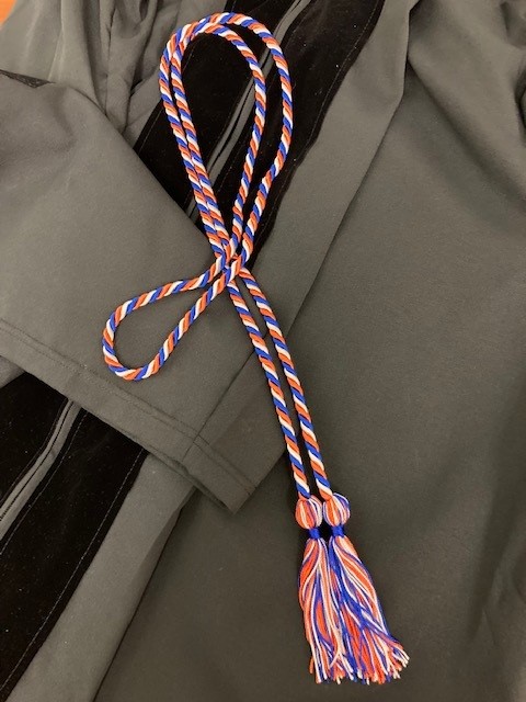 Blue, orange and white cords lying on a graduation gown
