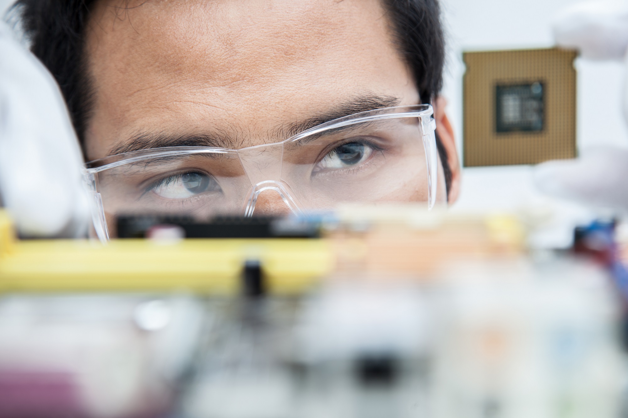 A lab technician with glasses looking at a microchip